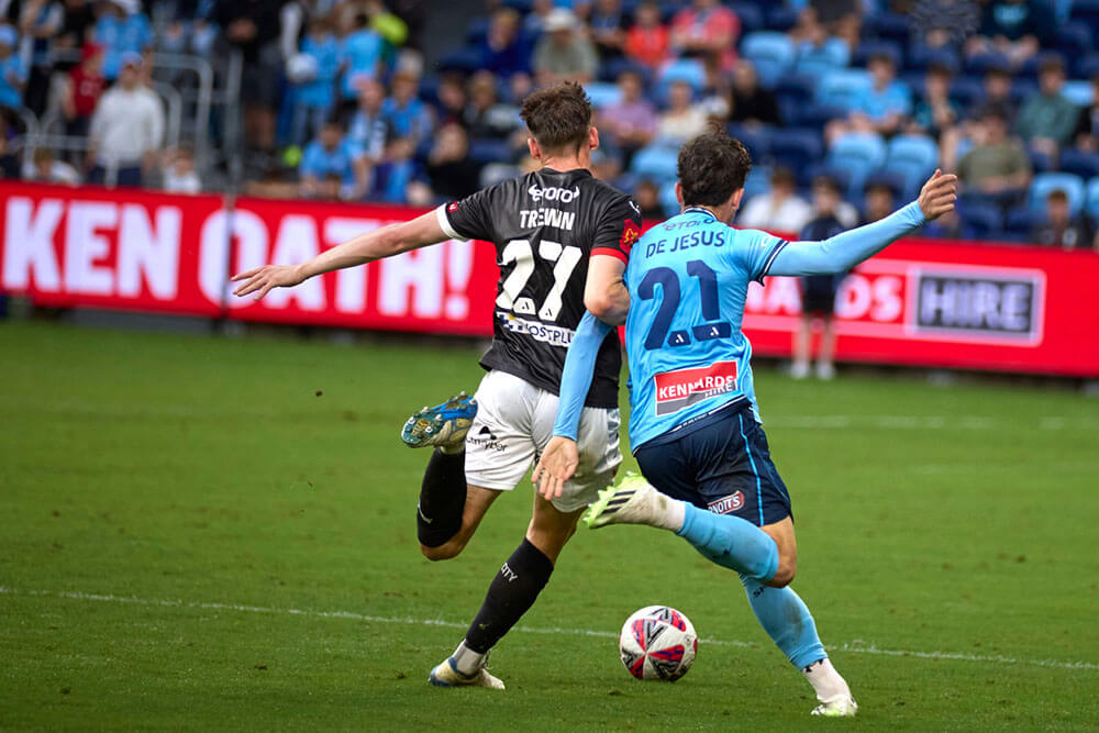 Sydney FC player and another player from another football team going after the ball on the pitch