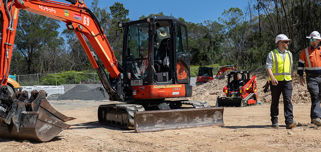 Kennards hire team member and site manager walking past a large excavator on site