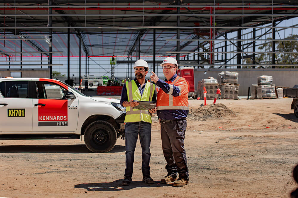 A Kennards Hire team member and site manager speaking to each other in front of a large scale construction site