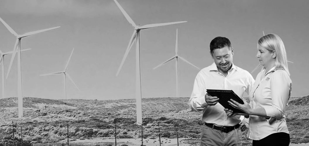 two people looking at a tablet with a wind farm in the background