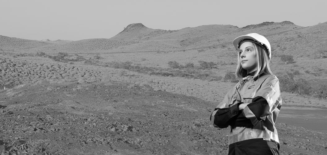 a person standing, arms crossed, with a mining site in the background